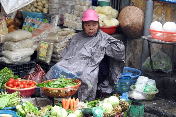 Deze groenteverkoper in Hanoi is gekleed op de regen en houdt zijn brommerhelm op als capuchon