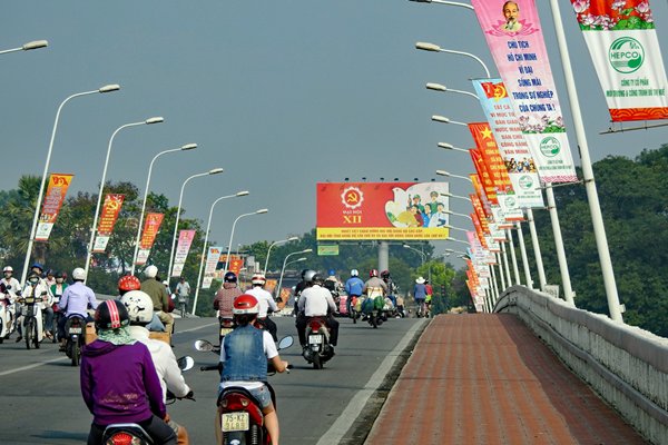 Drukke brug over de Parfum rivier met aan elke lantaarnpaal een spandoek, Hué (Vietnam)
