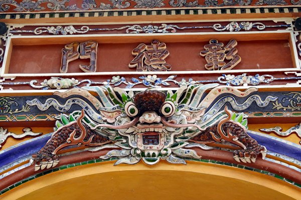 Monster met grote ogen in de daklijst van een poort in de citadel van Hué, Vietnam