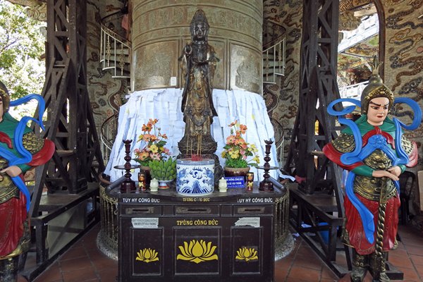 De donatiekist en een zuil vol wensbriefjes, geflankeerd door wachters in Trai Mat, Vietnam
