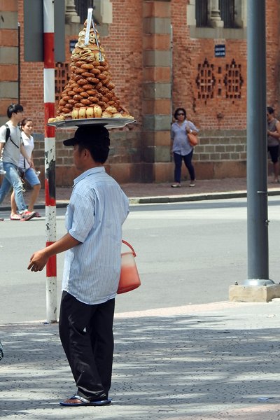 Straatverkoper in Saigon met een hoge last op zijn hoofd