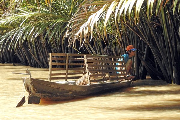 Bootje met schipper dat langs de dicht begroeide oever van de Mekong delta ligt